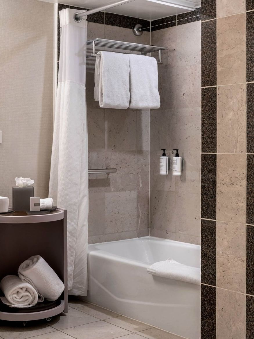 White towels on a shelf by a bathtub in a marble bathroom under soft light in Accessible Classic Rooms at Warwick Denver