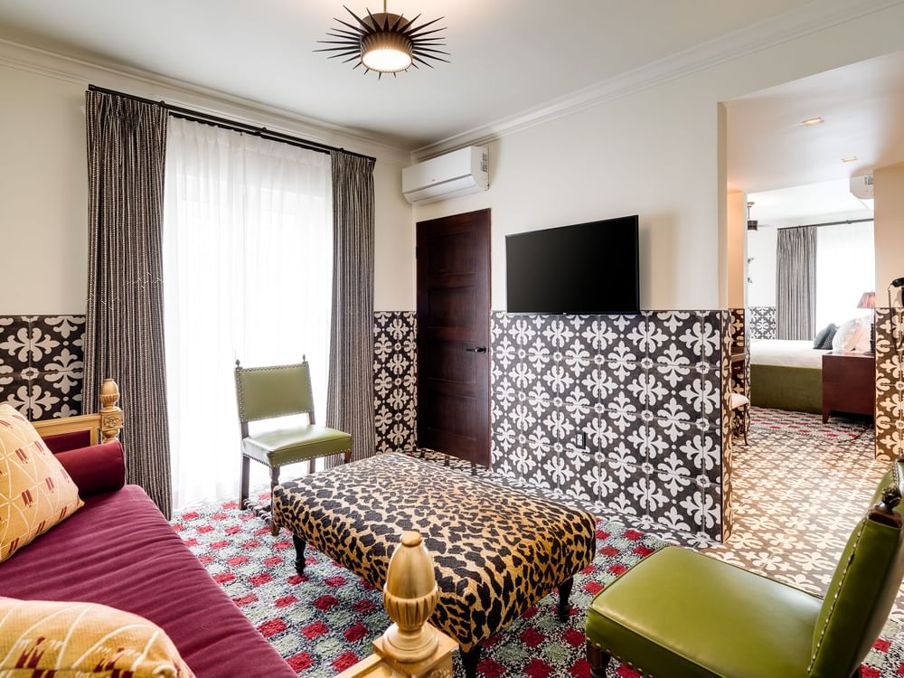 A wide view of a hotel room with a sofa, ottoman, TV, and chair.