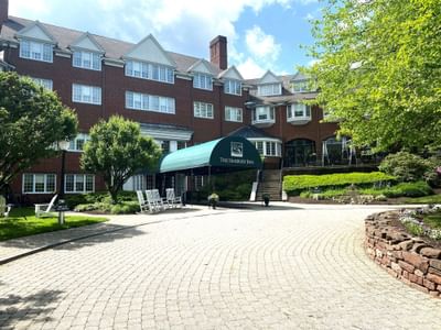 The Simsbury Inn brick building showing the green awning entrance with white rocking chairs and a paved courtyard path