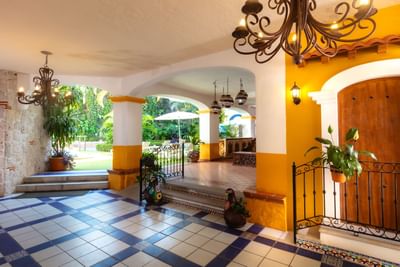 Vestíbulo colonial con arcos blancos y amarillos, lámparas de hierro forjado y vista al jardín en Los Arcos Suites
