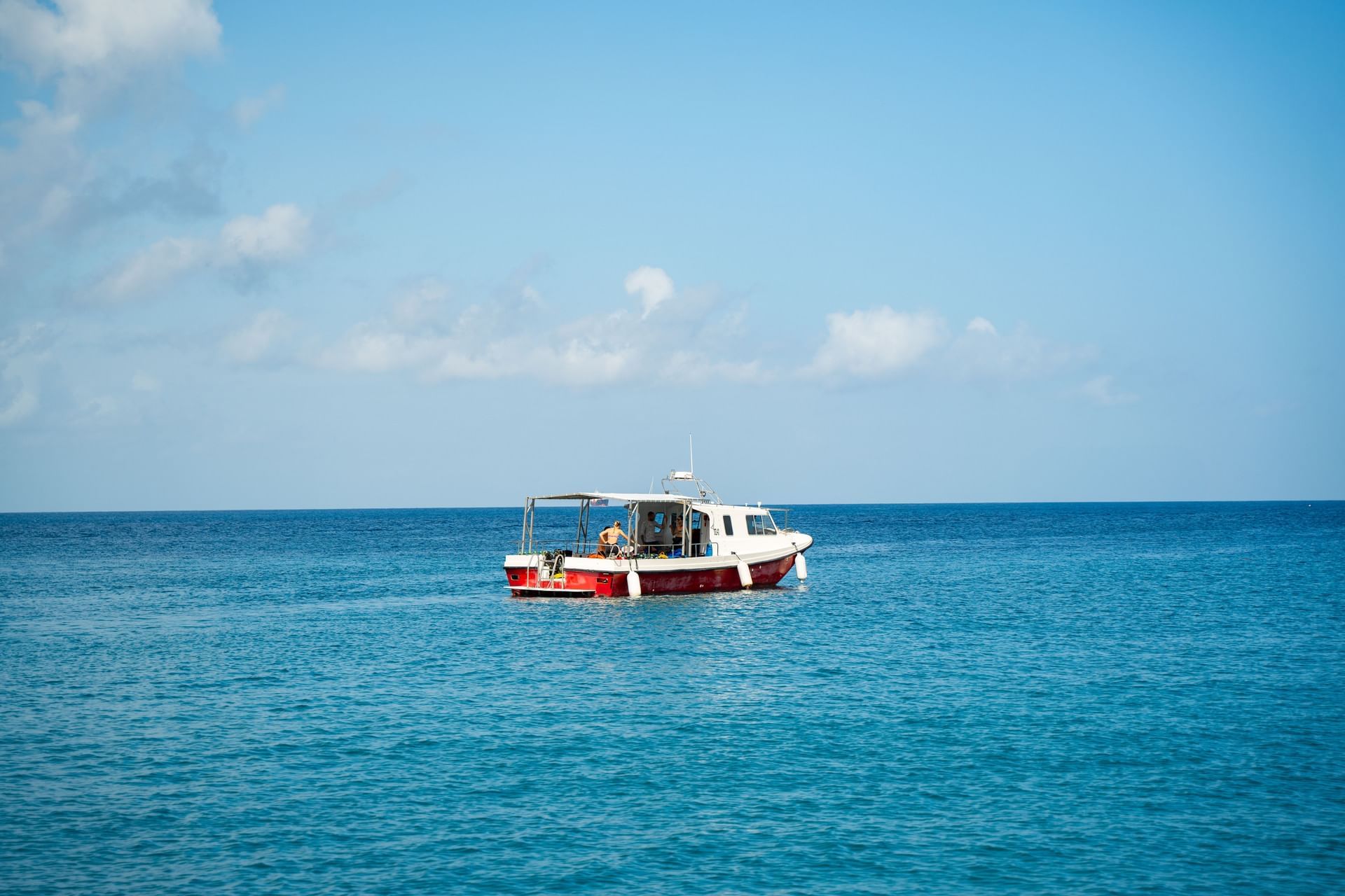 Persoon ontspant op een kleine wit-rode boot die drijft op kalm water onder een heldere hemel nabij Golden Rock Resort