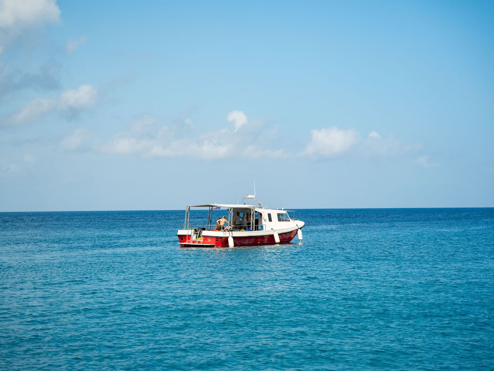 Person relaxing on a small white and red boat floating on calm water beneath a clear sky near Golden Rock Resort