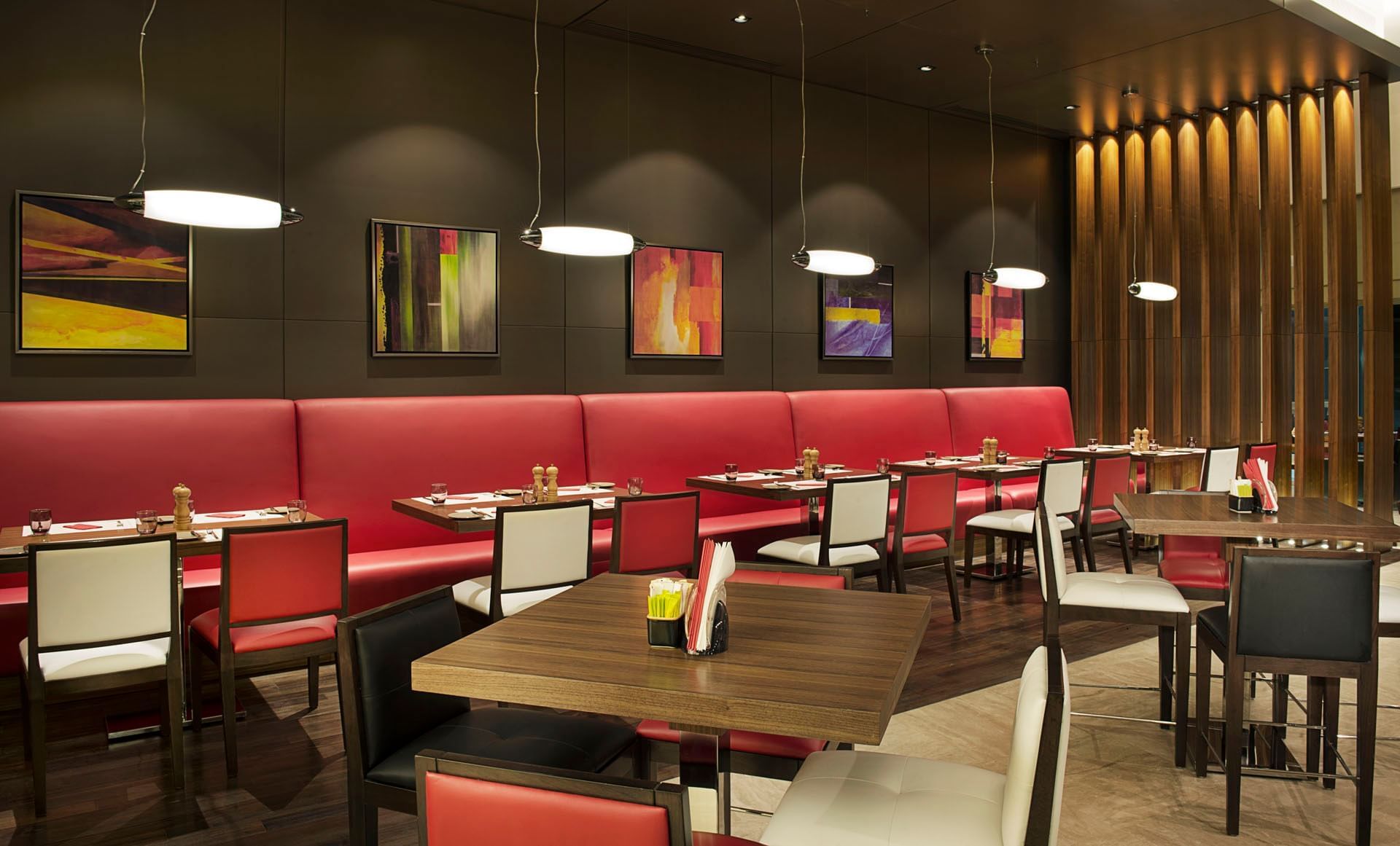 Modern interior with red booths, tables, pendant lights, and artwork in Maison Cafe, breakfast business bay at DAMAC Maison Cour Jardin