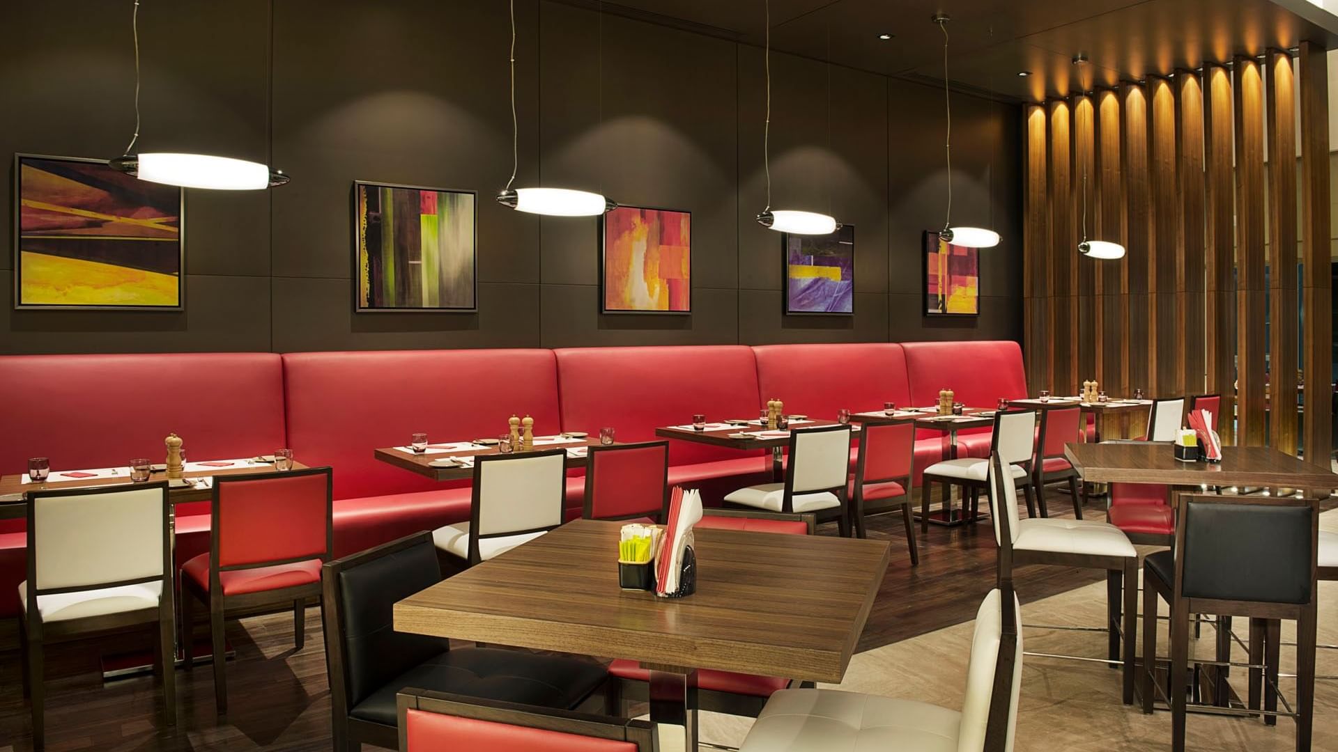 Modern interior with red booths, tables, pendant lights, and artwork in Maison Cafe, breakfast business bay at DAMAC Maison Cour Jardin
