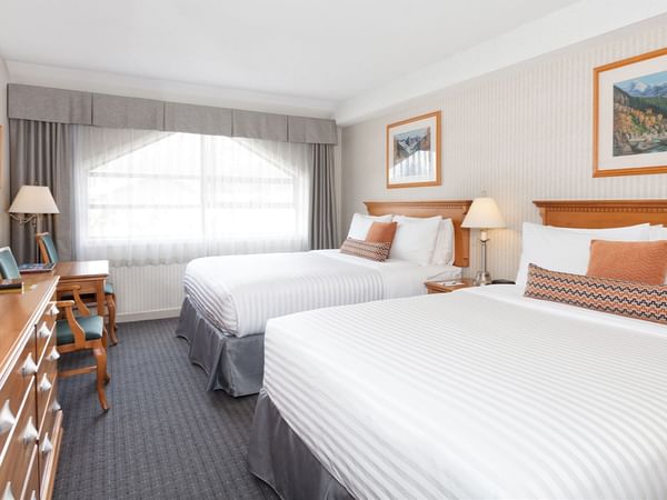 Spacious hotel room with two queen beds, elegant decor and large window for natural light.