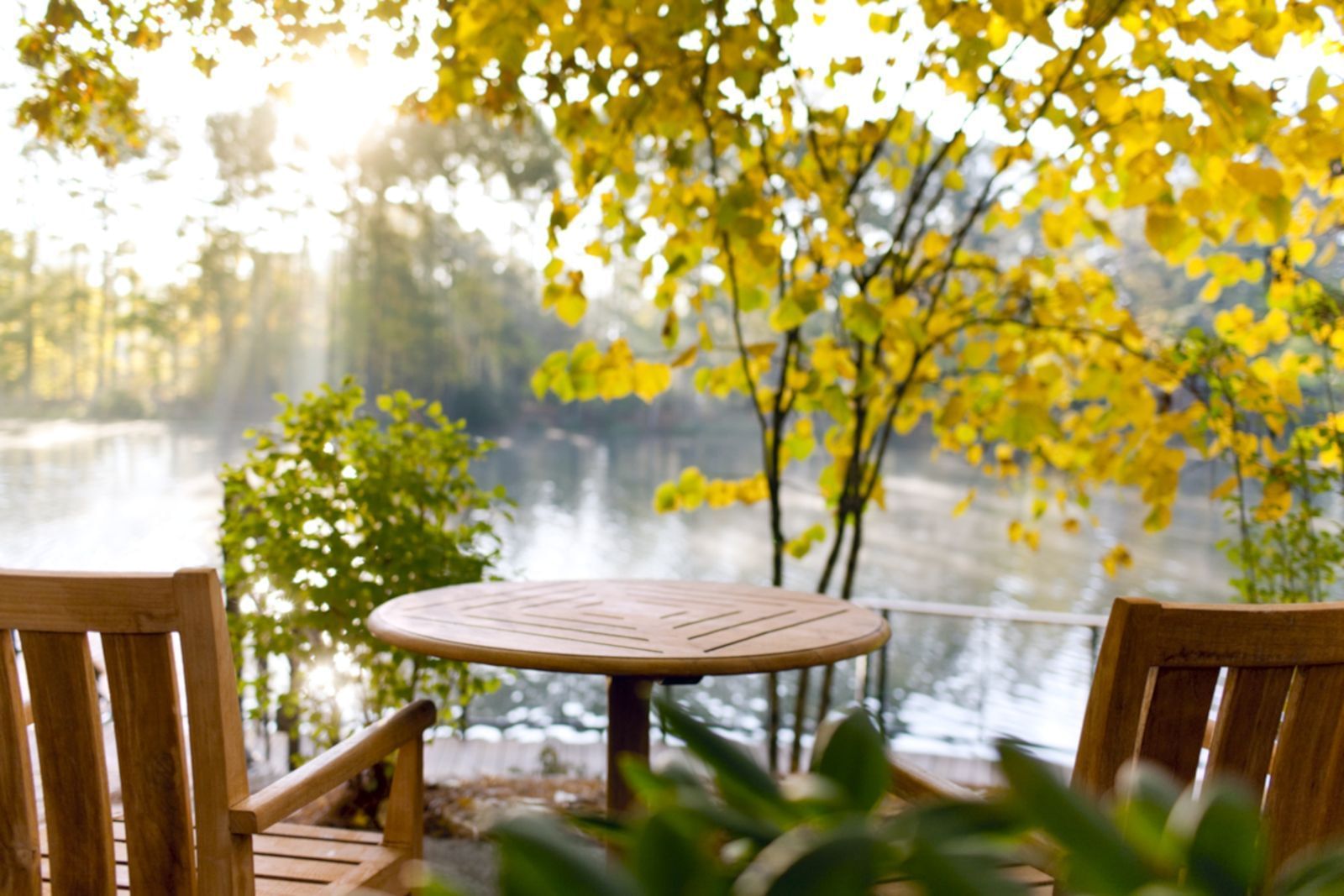 Two wooden chairs facing a table next to a scenic lake view at Umstead Hotel and Spa