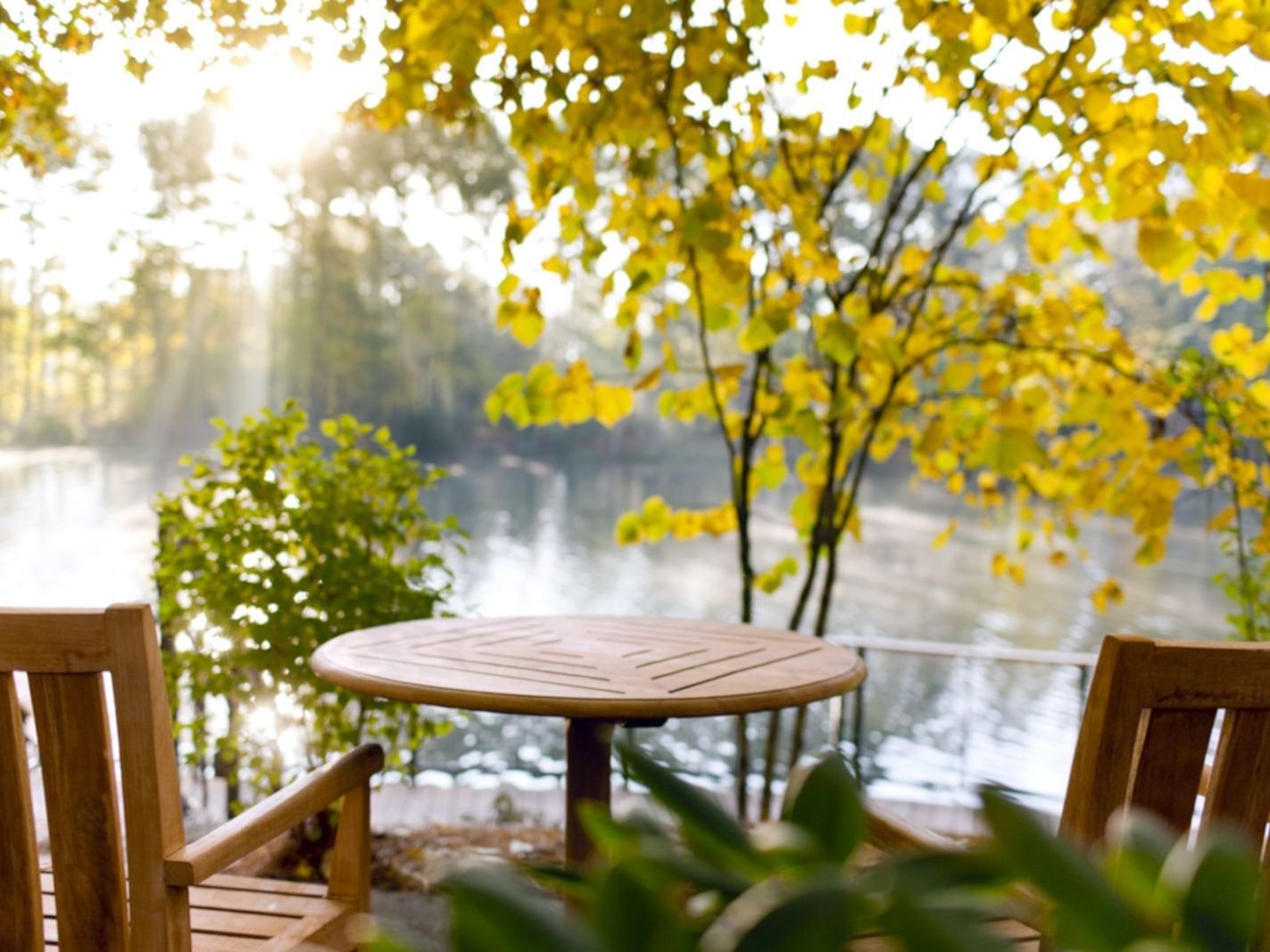 Two wooden chairs facing a table next to a scenic lake view at Umstead Hotel and Spa