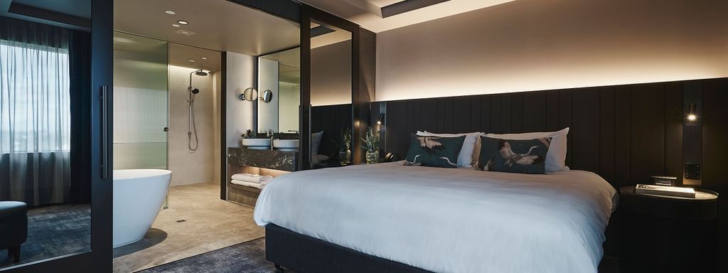 Spacious Deluxe Executive Suite with king bed, dark paneling, and open ensuite bathroom at Pullman East Melbourne