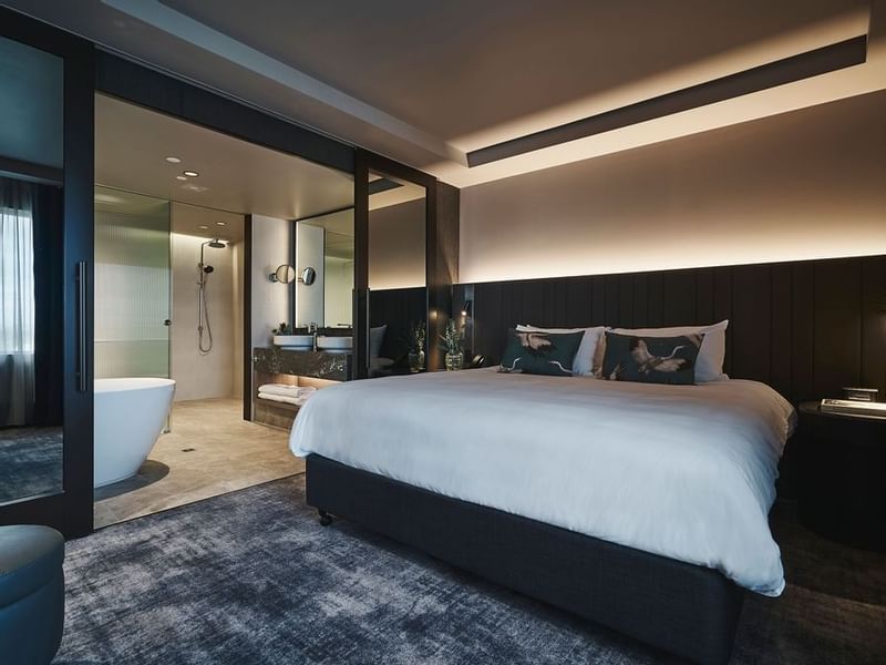 Spacious Deluxe Executive Suite with king bed, dark paneling, and open ensuite bathroom at Pullman East Melbourne