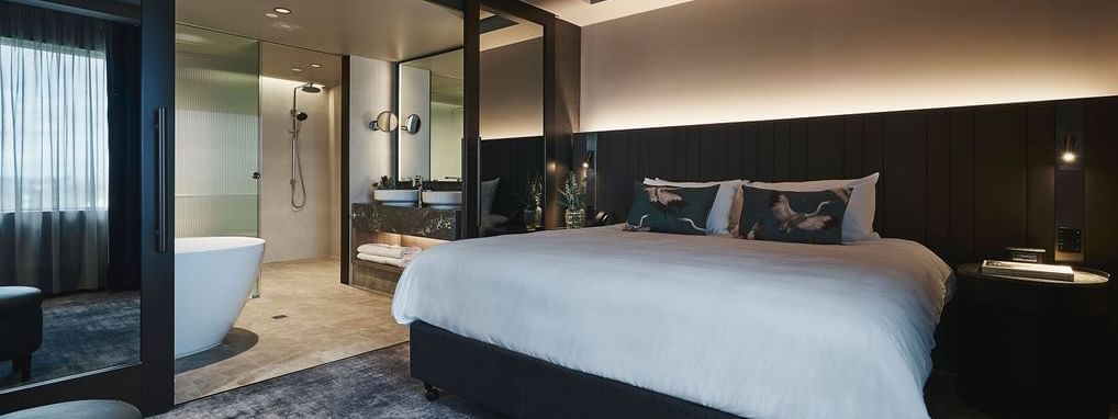 Superior Suite with king bed, dark wood paneling, ambient lighting, and ensuite bathroom at Pullman East Melbourne.