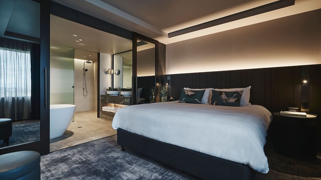 Superior Suite with king bed, dark wood paneling, ambient lighting, and ensuite bathroom at Pullman East Melbourne.
