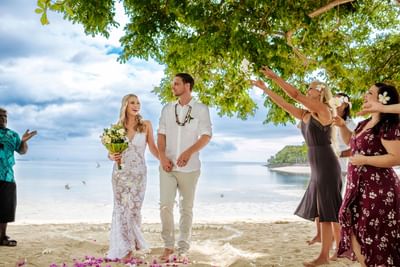 Beach wedding scene with a couple holding hands, and guests throwing petals at Musket Cove Island Resort & Marina