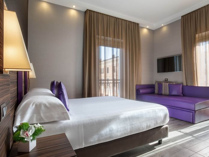 Family Room featuring a white bed with purple pillows, a purple sofa, and windows with sheer curtains at The Republic Hotel