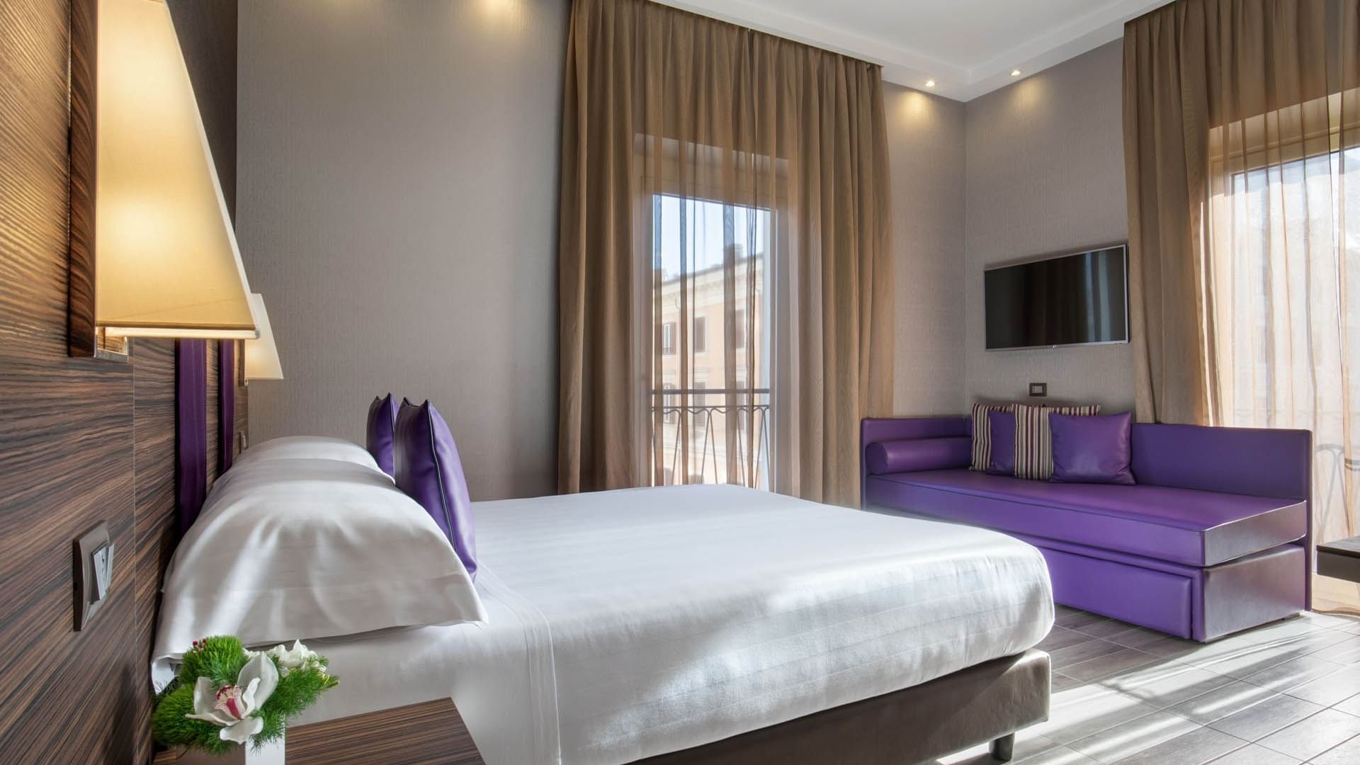 Family Room featuring a white bed with purple pillows, a purple sofa, and windows with sheer curtains at The Republic Hotel