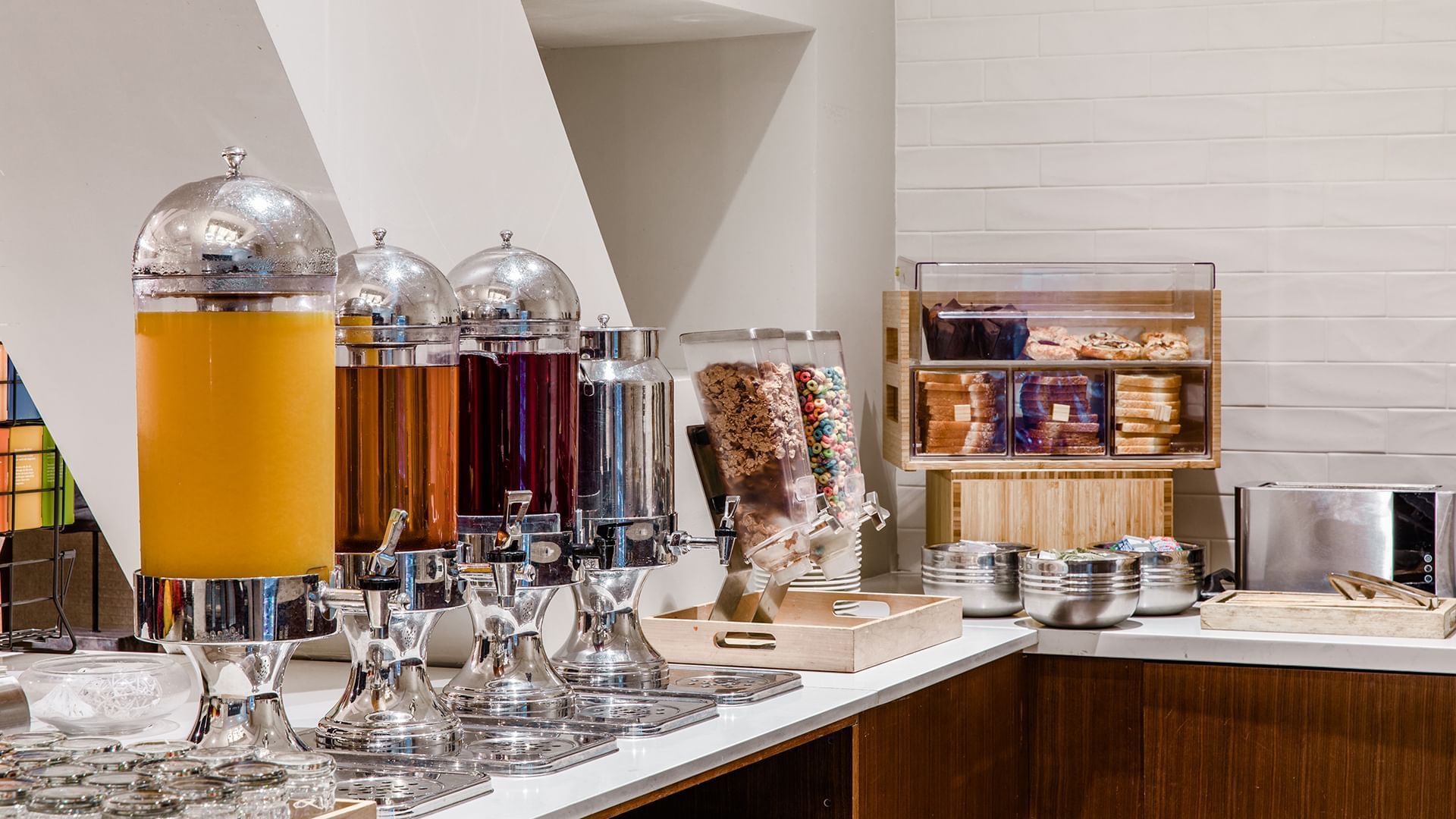 A breakfast buffet with juice dispensers, cereal dispensers, and pastries.