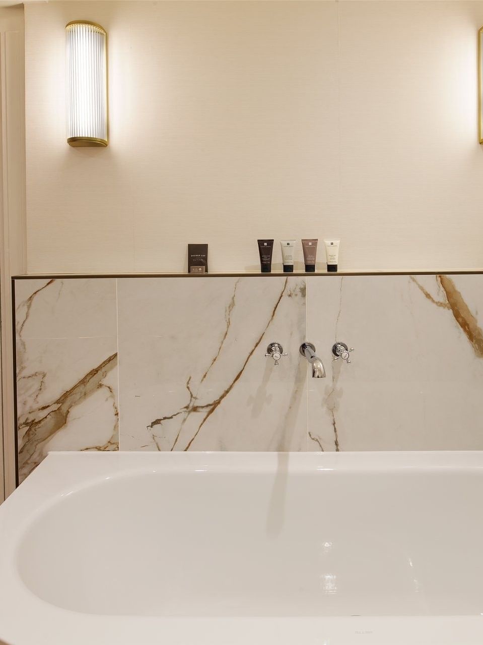 White bathtub with marble wall and modern fixtures in a suite at The Capital Hotel, Apartments & Townhouse