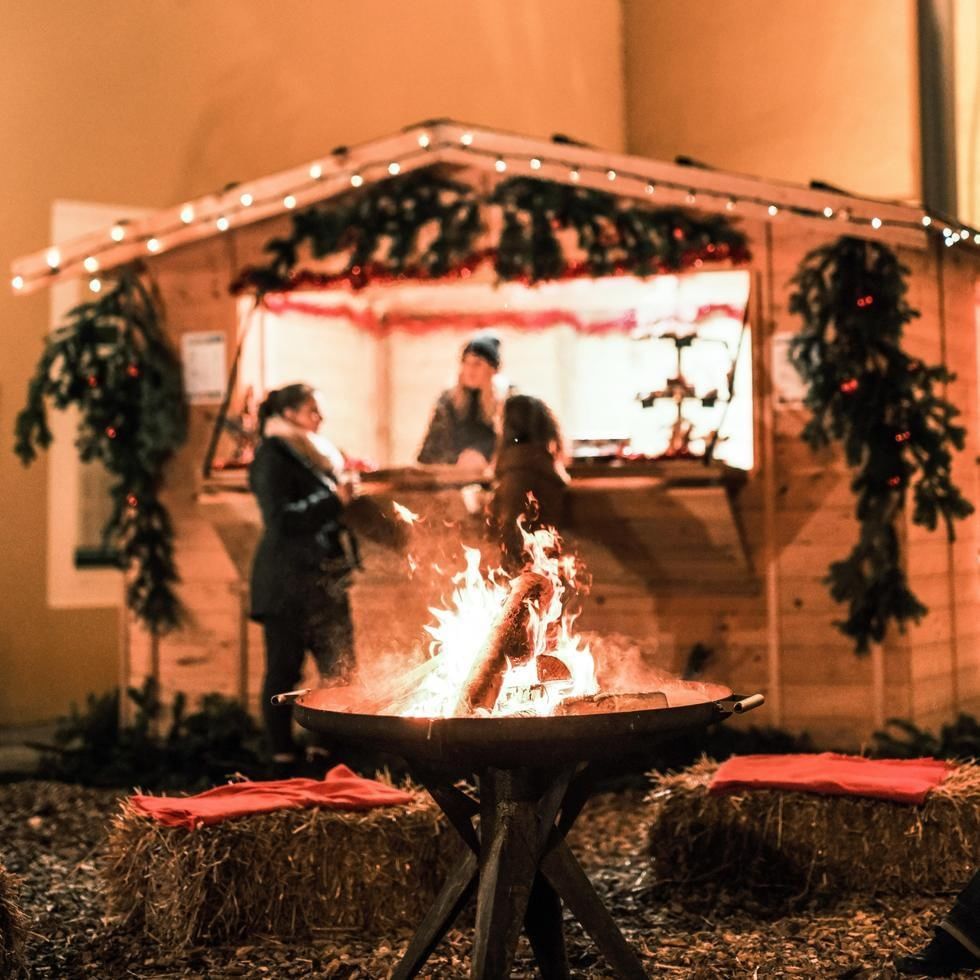 Persone intorno a un falò di fronte a una capanna decorata con luci e ghirlande natalizie.