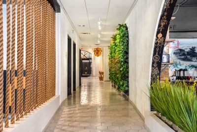 Stylish hallway at The Riverwalk Plaza Hotel featuring rope dividers, lush greenery, and tile flooring leading to the lobby