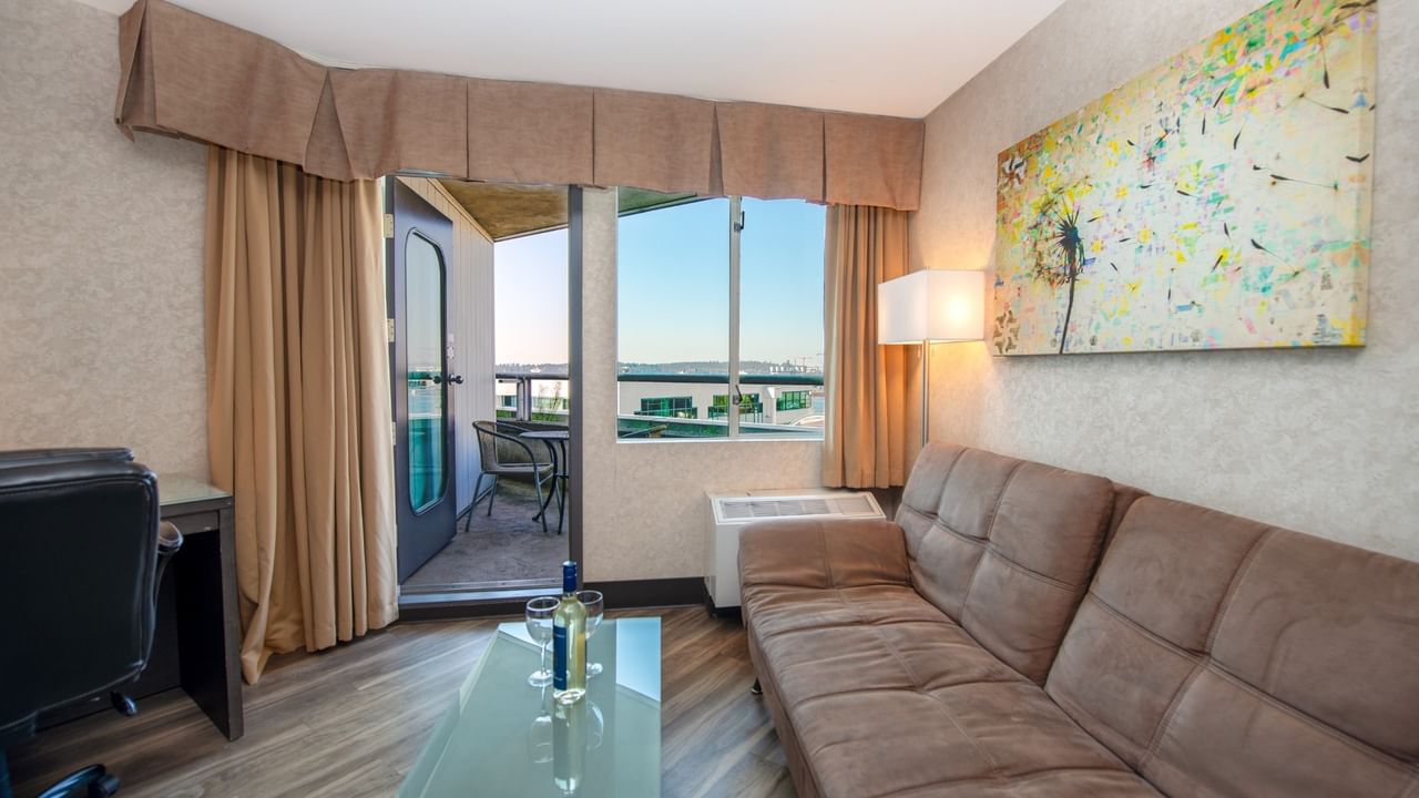 Coast Premium King with Patio with a couch, glass table, balcony, desk, and abstract painting at Coast Lonsdale Quay Hotel