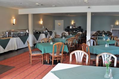 Fox Ridge Resort dining hall with multiple tables covered in green cloth, chairs, and decorative flowers in vases.
