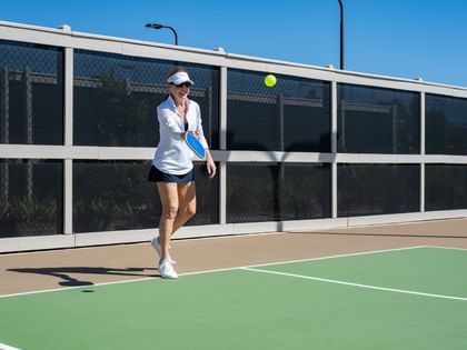 Woman playing pickleball on an outdoor court under a clear blue sky at Camp Creek Inn in Inlet Beach
