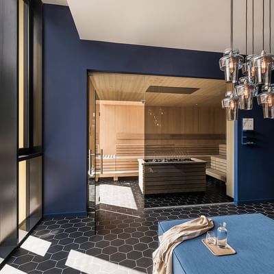 Blauer Raum mit Sauna, Holzbänken, schwarzem Sechseckboden und hängenden Leuchten.