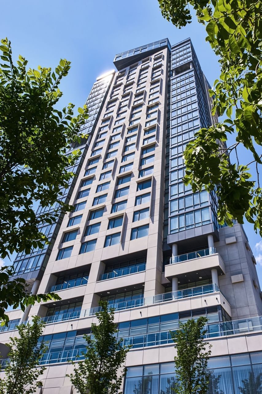 Tall modern glass hotel building facing blue sky framed by green tree branches in foreground at Hotel X Toronto hotel