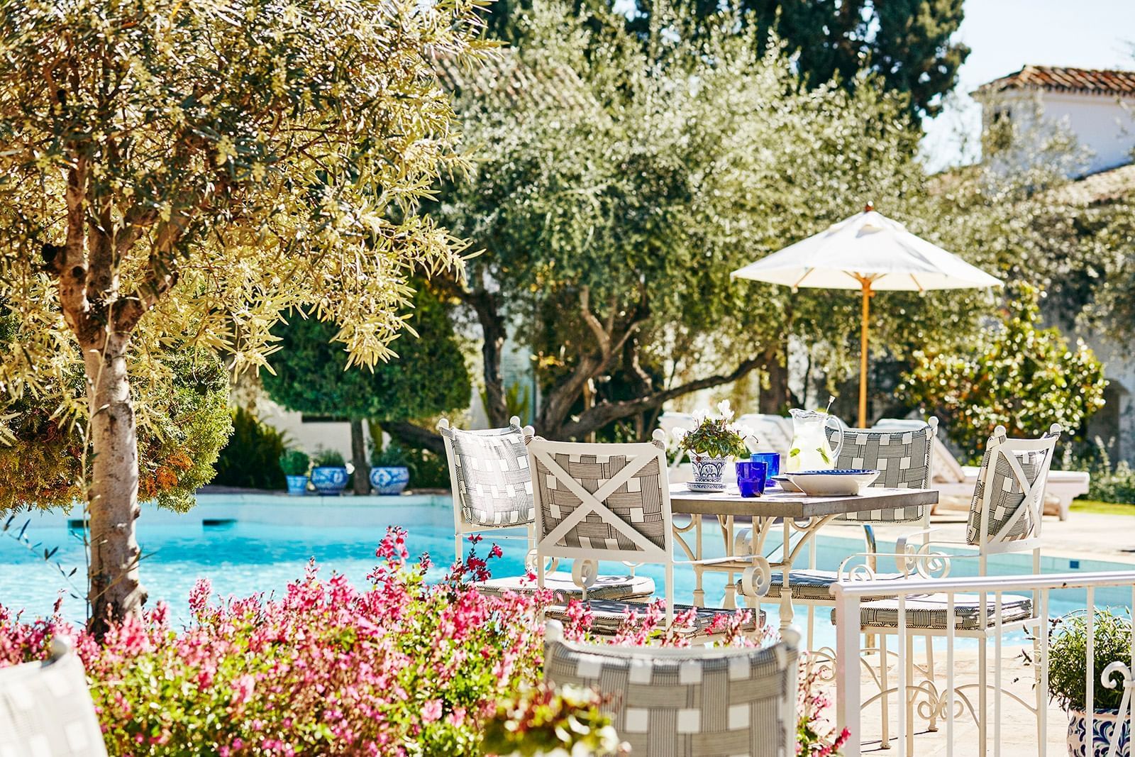 Sunlit Marbella Club poolside patio with chic dining furniture, lush greenery, and vibrant pink blooms
