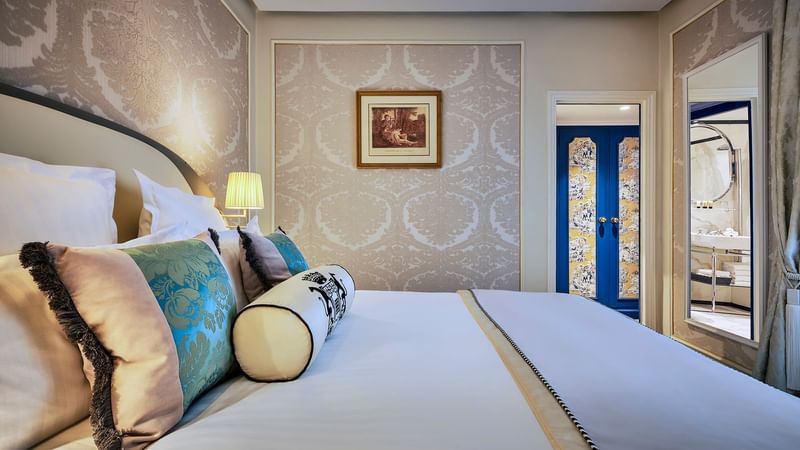 Deluxe Room featuring plush pillows, a lamp, and a door leading to a bathroom at Hôtel Westminster - Paris