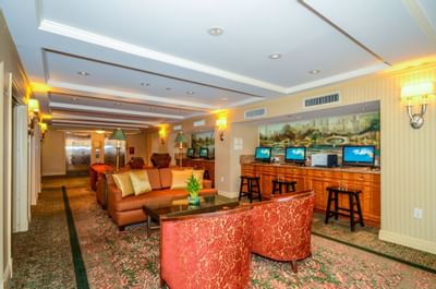 Lounge area with red chairs, coffee table, couch, and bar with computers, in a hotel.