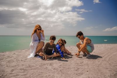 Family of four relaxing on white sand beach with turquoise water under cloudy skies at Playa Blanca Beach Resort