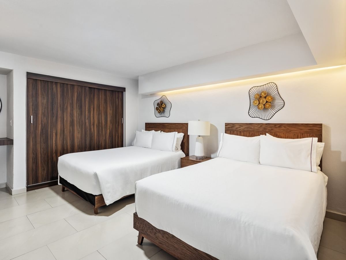 Junior Suite Vista Parcial Al Mar with two white-linen beds, decorative wall art, and a dark wood door at Sunvivia Mazatlán