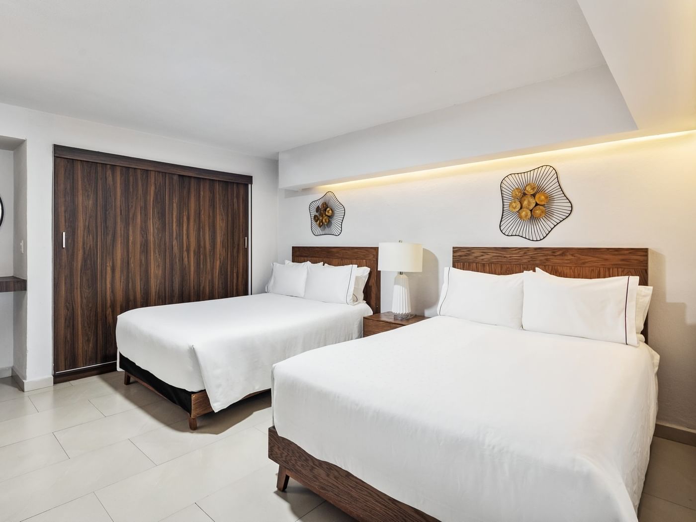 Junior Suite Vista Parcial Al Mar with two white-linen beds, decorative wall art, and a dark wood door at Sunvivia Mazatlán