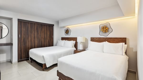 Junior Suite Vista Parcial Al Mar with two white-linen beds, decorative wall art, and a dark wood door at Sunvivia Mazatlán