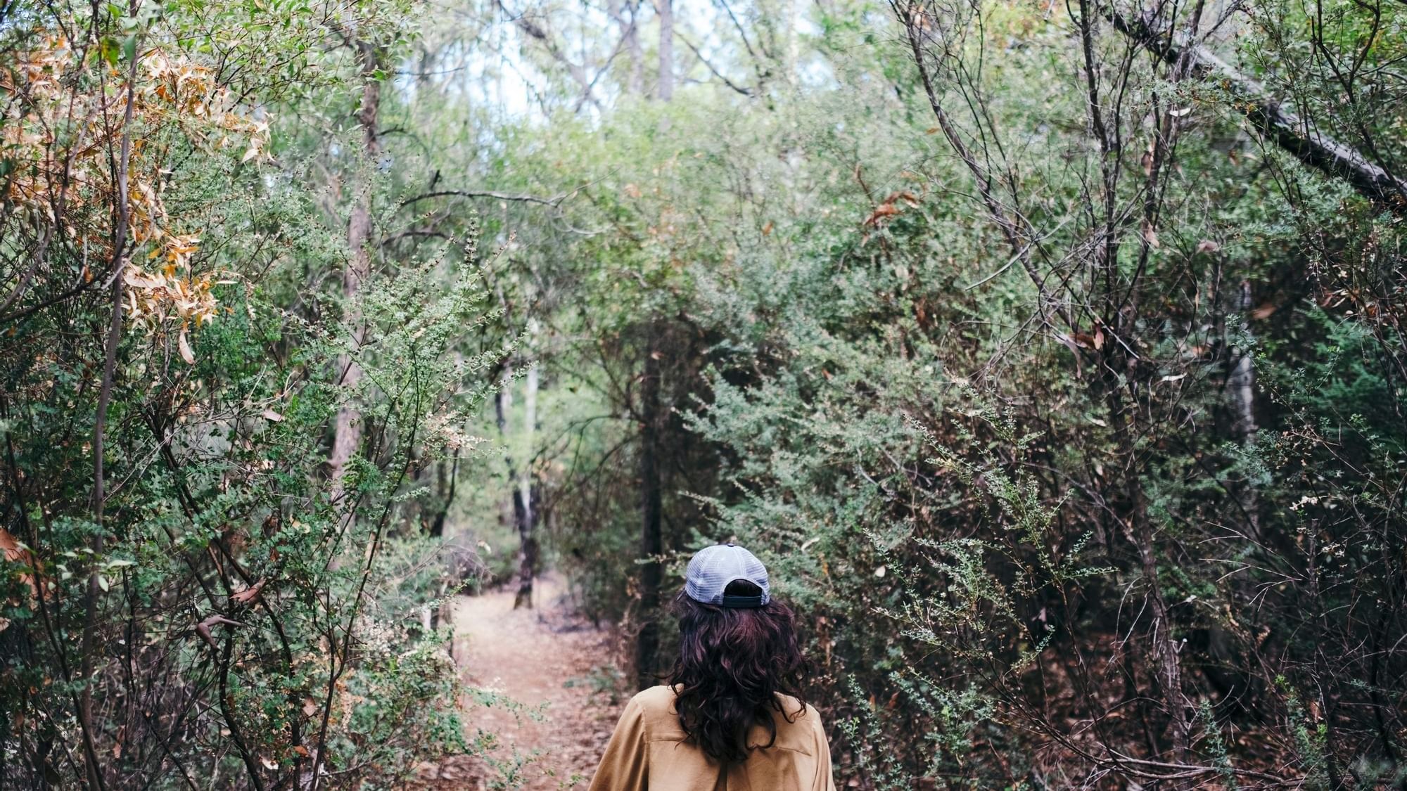 A woman walks along a dirt path through a dense green forest near The Sebel Mandurah