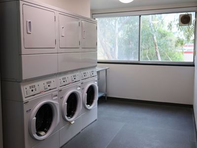 Multiple washers and dryers lined up in a laundry room at La Trobe University – Menzies College.