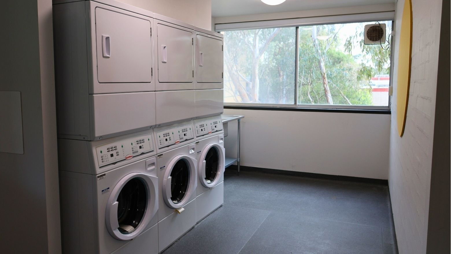 Multiple washers and dryers lined up in a laundry room at La Trobe University – Menzies College.
