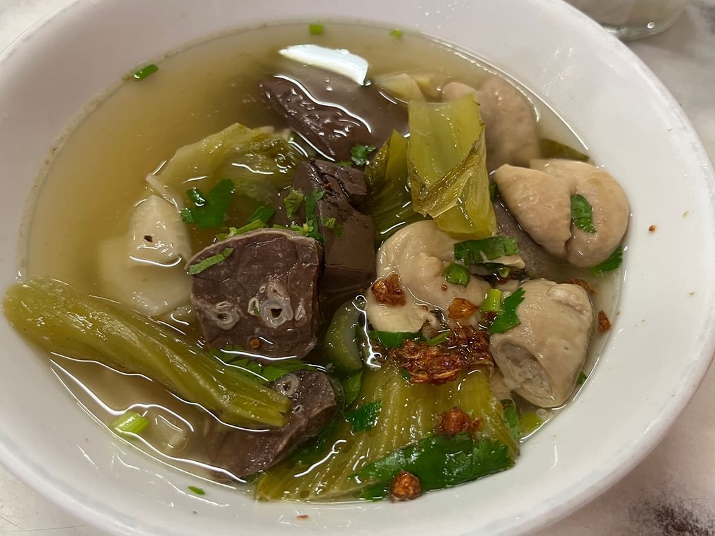 Bowl of clear soup featuring chunks of cooked meat, leafy greens, and chopped herbs in Yok Keng at Hop Inn Surat Thani