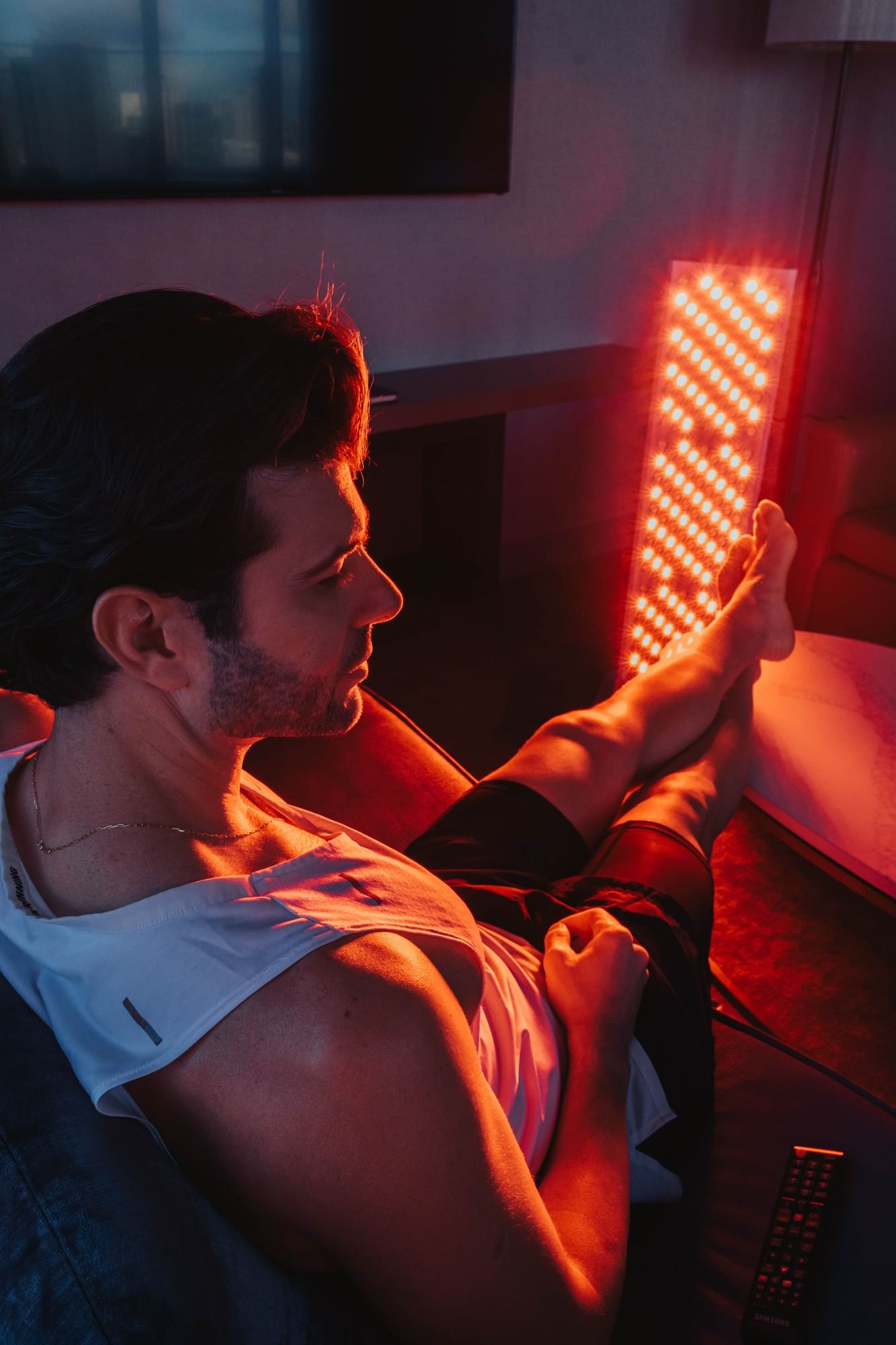 Man resting his feet on a glowing red light therapy panel, beside a couch in his suite at Hotel X Toronto