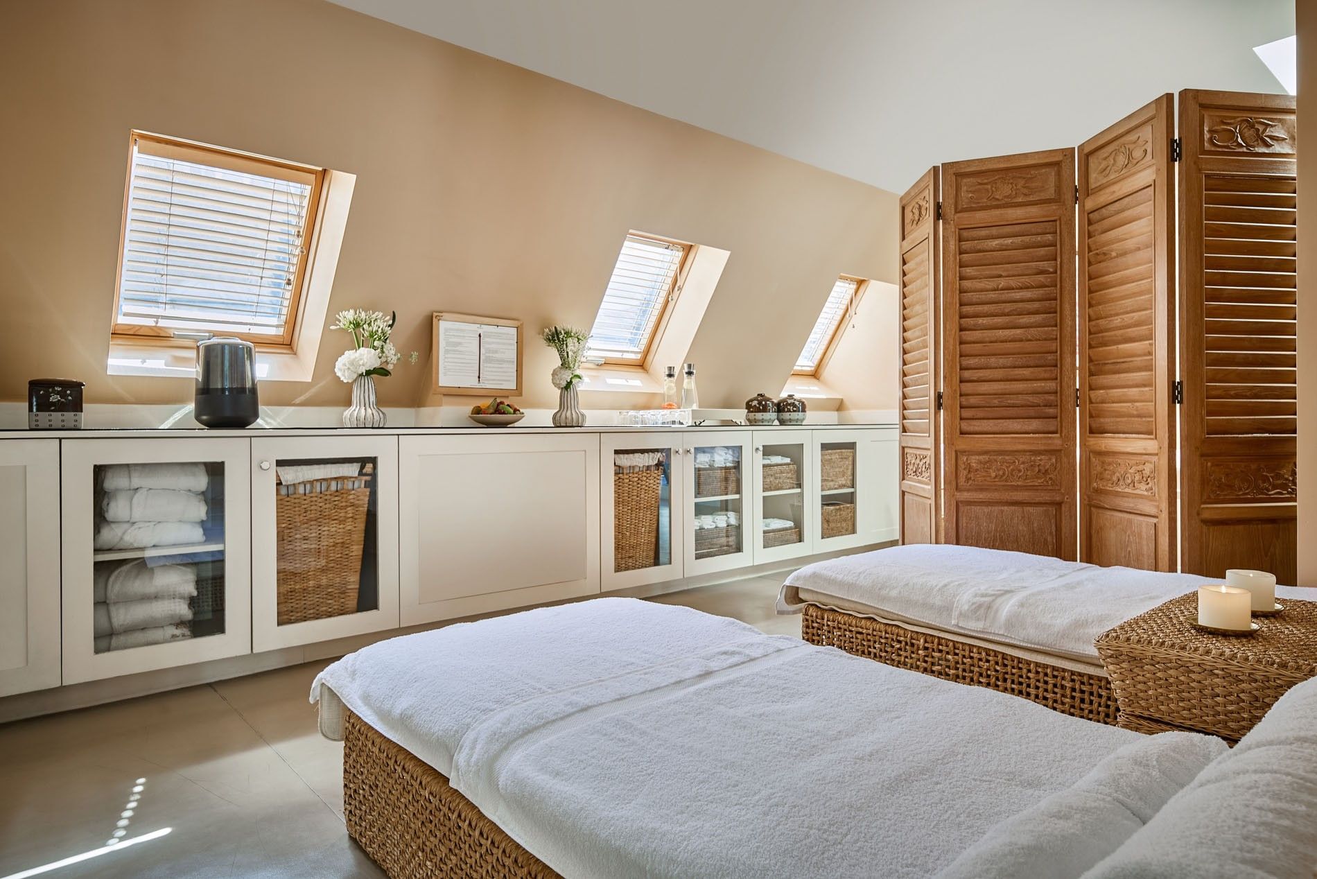 Salle de soins lumineuse avec deux tables de massage en rotin sous fenêtres de toit à Hotel Westminster Warwick Paris