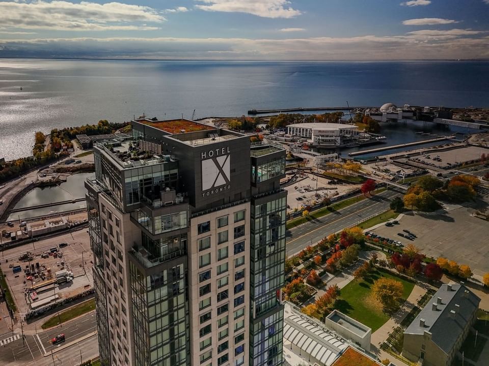 Vue aérienne de l'hôtel X Toronto au bord d'un lac avec des arbres d'automne et un ciel dégagé.