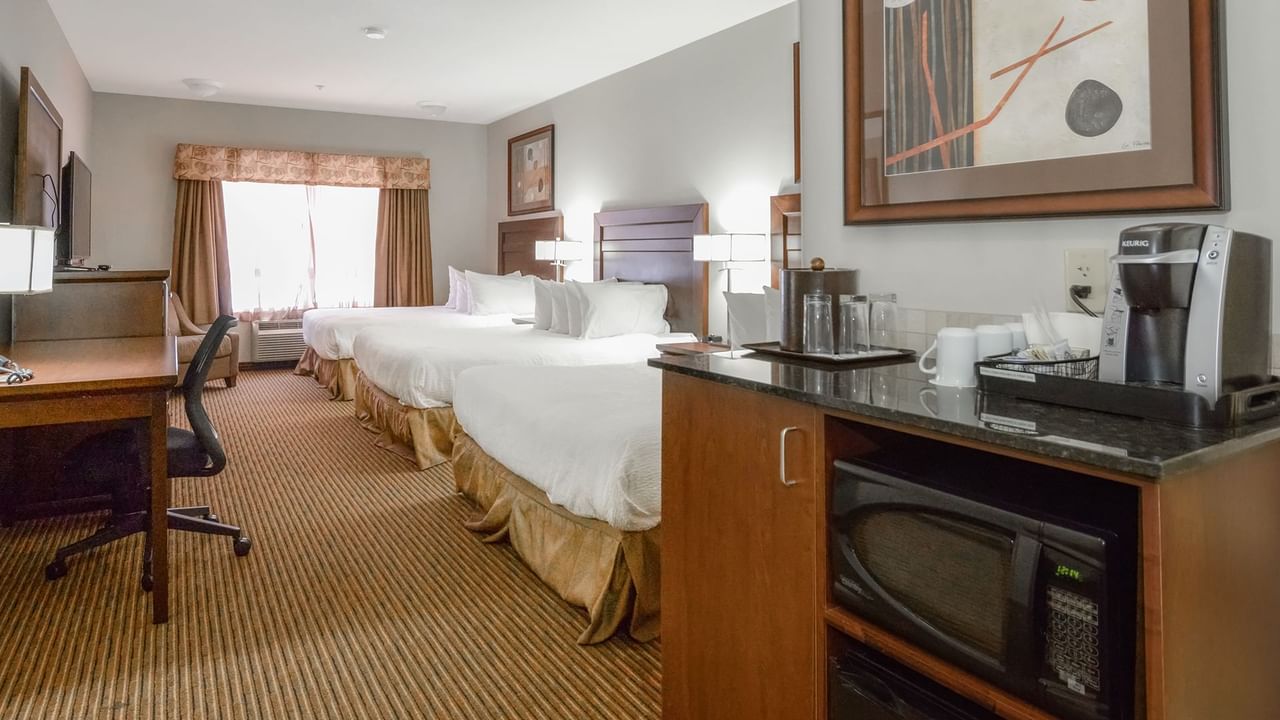 Hotel room with three queen beds, microwave, TV, work desk and coffee machine