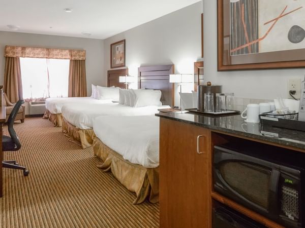 Hotel room with three queen beds, microwave, TV, work desk and coffee machine
