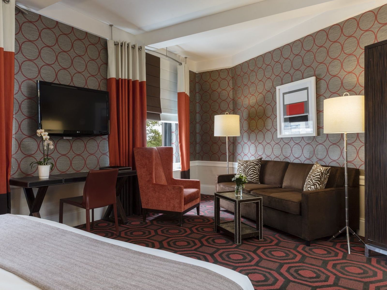 Stylish NYC hotel room with chair, sofa, desk, wall mounted TV, fresh orchid, and midcentury modern design