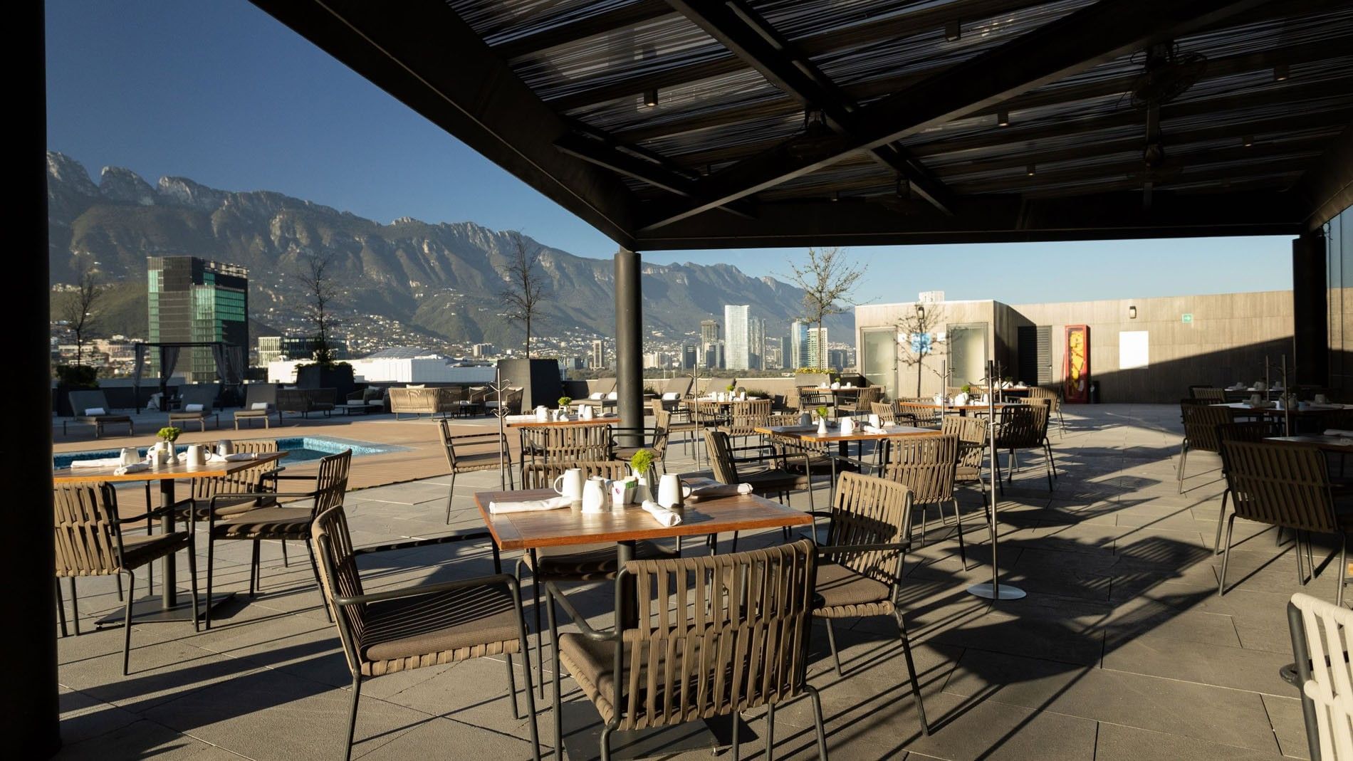 Outdoor hotel restaurant patio with wooden tables under a shaded structure at Camino Real Fashion Drive, Monterrey