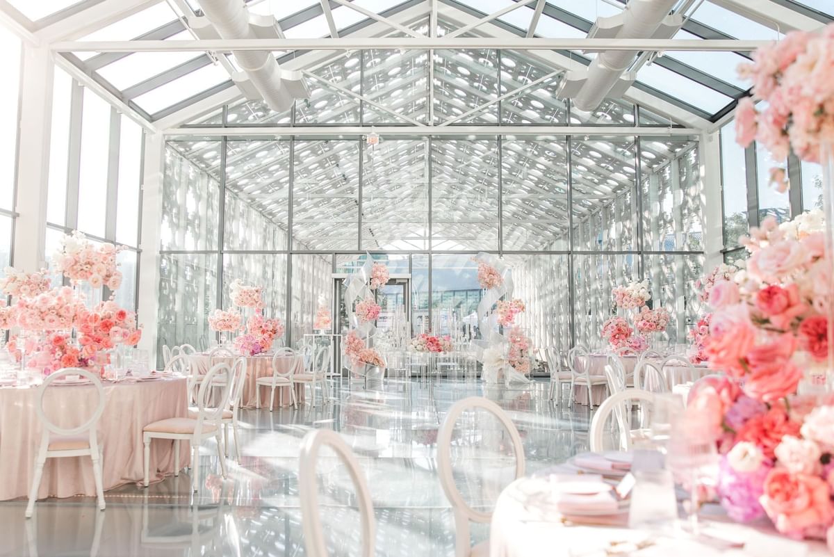 Bright glass greenhouse wedding venue with round tables and pink floral centerpieces and clear chairs at Hotel X Toronto