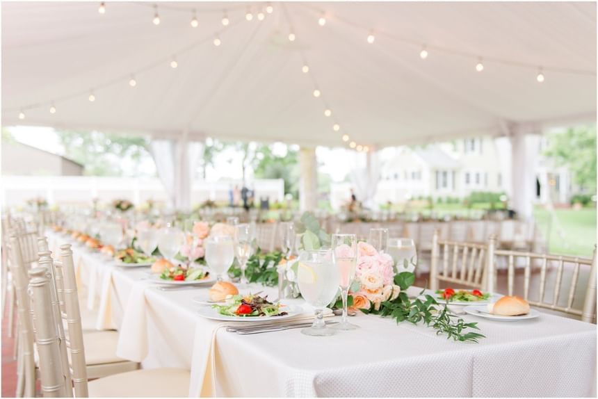 Elegant outdoor tent reception with long tables, and gold chiavari chairs at Aramark Chauncey Conference Center