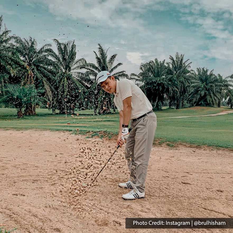 Golfer swinging club in sand bunker on a palm-lined course - Lexis Port Dickson