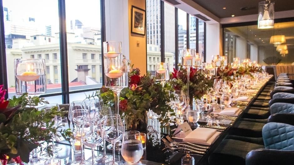 Elegant dining setup with lit candles on a long table with a city view in Prive at Sofitel Brisbane Central