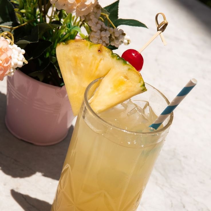 a yellow cocktail with a pineapple wedge and cherry garnish